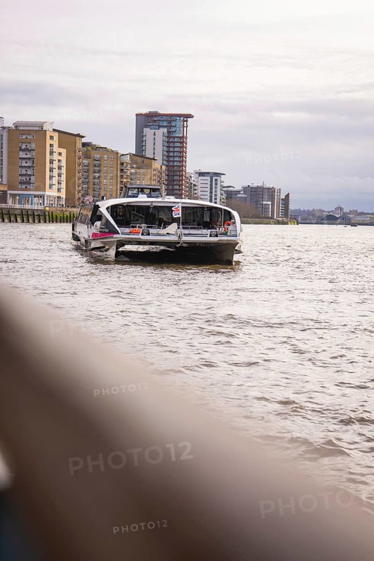 A boat on a wide river with modern buildings in the background and a cloudy sky, London, England, Great Britain