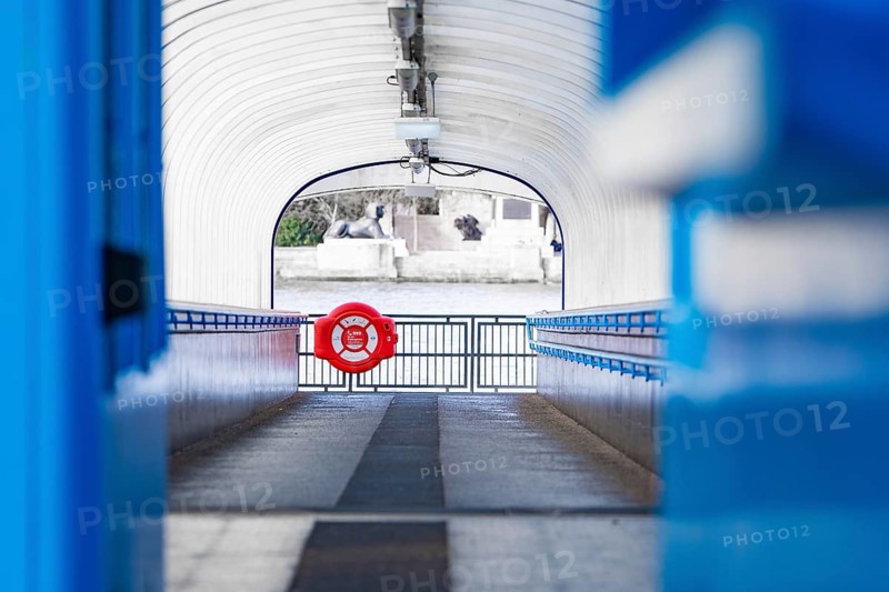 A modern passageway leads to a river, accented with a blue lifebuoy, London, England, Great Britain