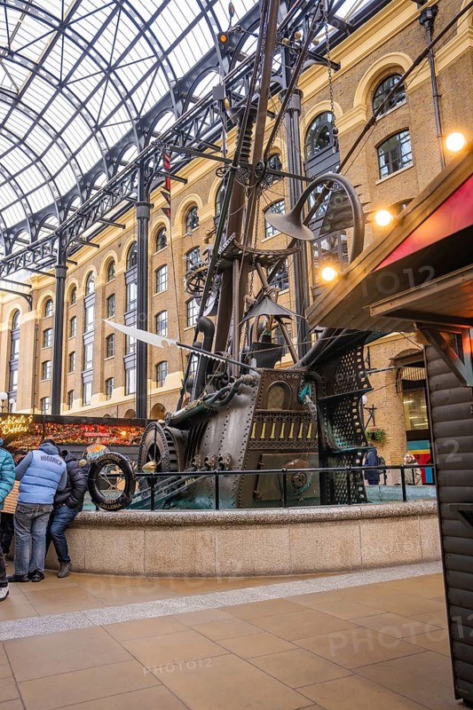 A large metal sculpture in a covered interior surrounded by people, The Navigators, London, United Kingdom