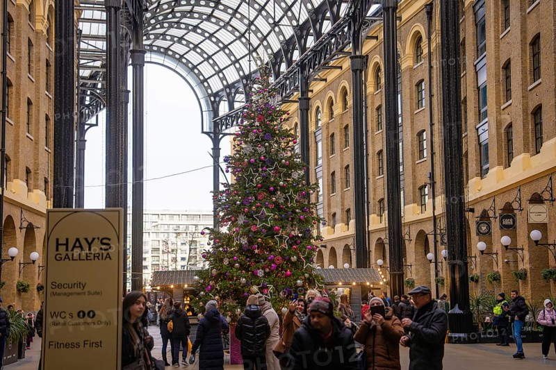 Christmassy decorated gallery with large Christmas tree surrounded by shops and people, London, United Kingdom