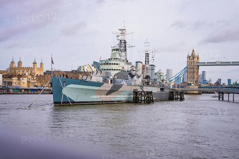 Large historic ship on the river in front of a bridge, with city skyline and towers on the horizon, HMS Belfast, London, United Kingdom