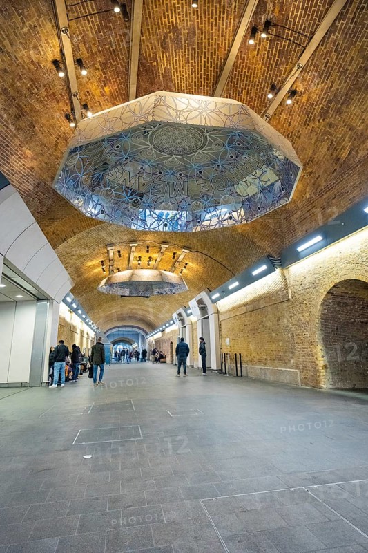 Long tunnel with decorative ceiling and people, warm lighting in an urban setting, London Bridge Station, London, United Kingdom