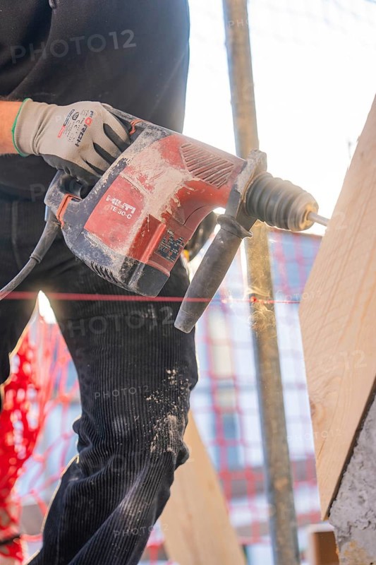 A worker is drilling wood with a red electric drill on a construction site. Dust flies up, carpentry construction site, roof extension, renovation, Stuttgart, Germany