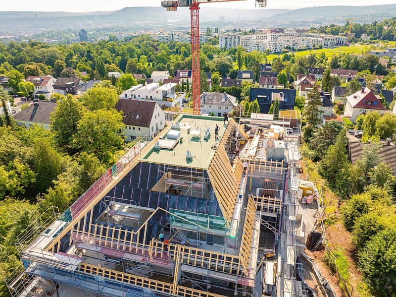 A new building with a construction crane in a residential area, surrounded by green vegetation and city views, carpentry construction, roof extension, renovation, Stuttgart, Germany