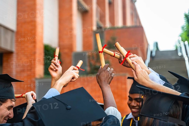 Diverse group of university students wearing graduation caps and gowns, celebrating their achievement and success while holding their diplomas joyfully in the air after completing their education