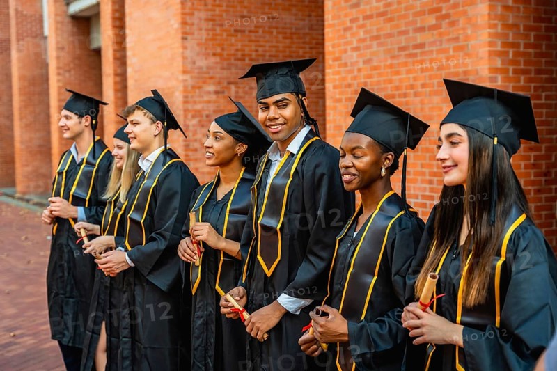 Diverse group of young students and graduates wearing academic regalia or cap and gown, smiling and holding their diplomas, celebrating graduation on university campus
