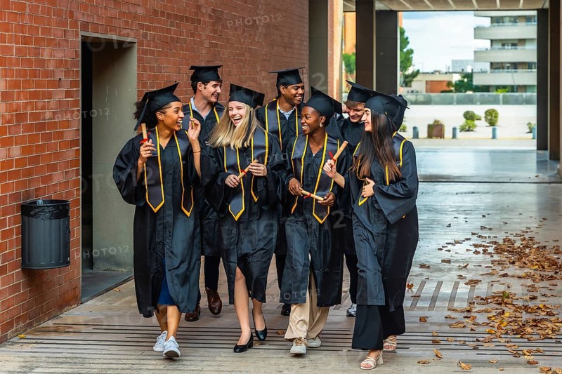 Diverse group of happy graduates celebrating achievement, walking on campus wearing academic gowns, caps, and holding rolled diplomas after finishing university education