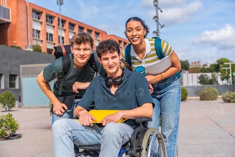 Happy young students, including a person using a wheelchair, standing together on a university campus, representing diversity, inclusion, and friendship in education