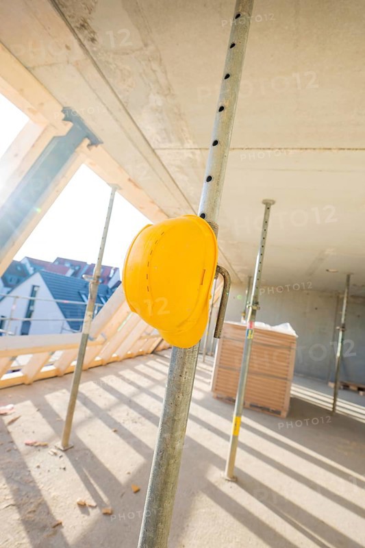 A yellow safety helmet hangs on a metal support on a construction site in sunlight, carpentry construction, roof extension, renovation, Stuttgart, Germany