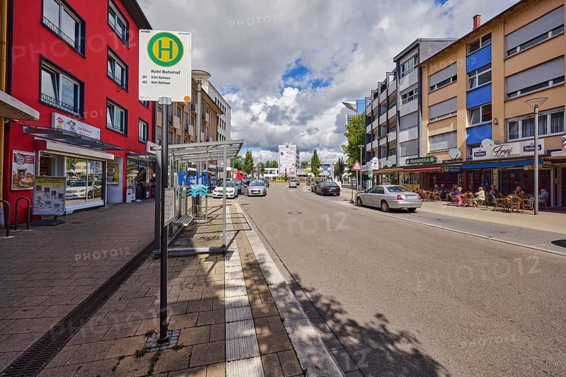 Bus stop Kehl station, bus shelters, general architecture, houses, row of houses, residential buildings and commercial buildings, shops, retail, parking strips with vehicles, outdoor area of a restaurant, bistro, café, pub, blue sky, cumulus clouds, main street, Kehl, Upper Rhine Plain, Ortenau district, Baden-Württemberg, Germany