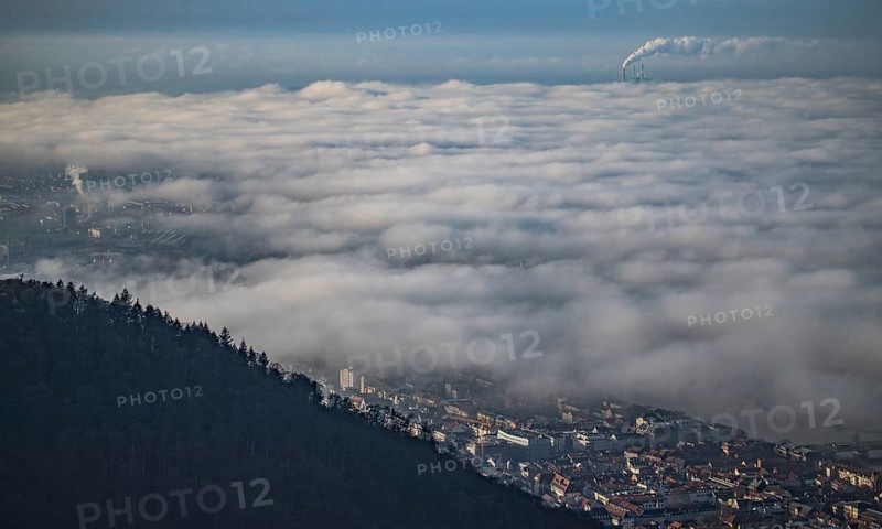 Aerial view of the city of Heidelberg on the Neckar, fog landscape of low-hanging clouds and fog fields that float and swirl above the roofs of the city with large and smoking chimney vents sticking out of the fog in the background, Heidelberg, Baden-Württemberg, Germany