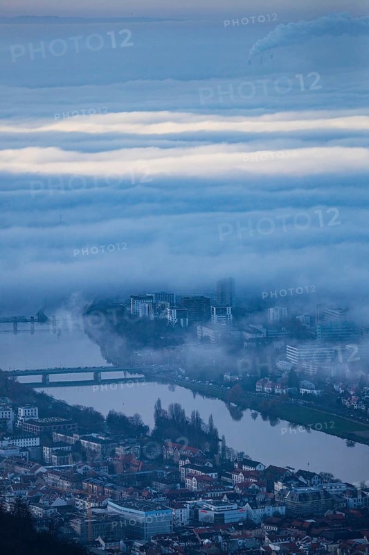 Aerial view of the city of Heidelberg on the Neckar, sea of fog from low-hanging clouds and fog fields, sunlit above the roofs of the city and the Neckar river, floating and waving with large and smoking chimney vents sticking out of the fog in the background, Heidelberg, Baden-Württemberg, Germany
