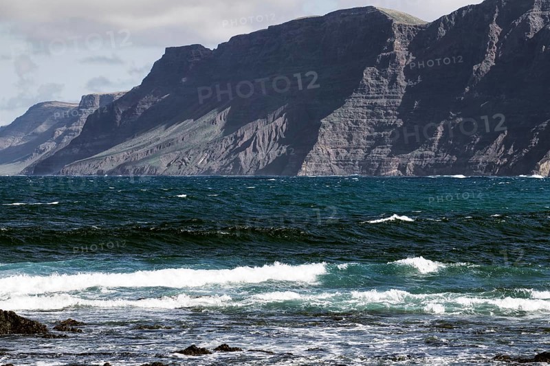 Coast with thundering waves and high mountains in the background Risco de Famara) under partly cloudy sky, Playa Caleta de Famara, Teguise Lanzarote
