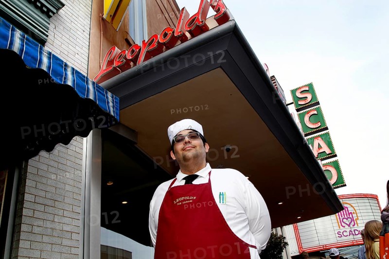 Ice cream parlour worker in uniform poses smiling in front of Leopold's ice cream parlour with retro animated signs, Savannah, Georgia, USA