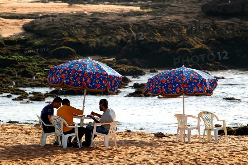 Group of people sitting under colorful umbrellas on Oulidia beach, Oulidia, Morocco