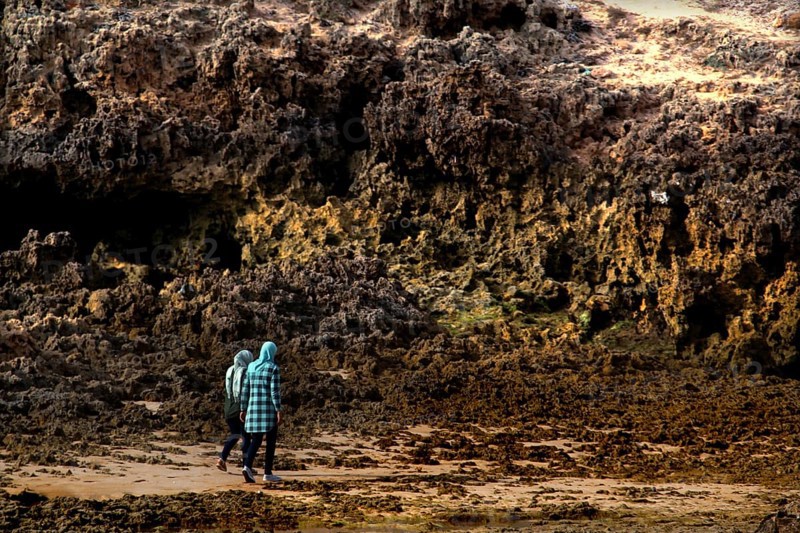 Person walking along rocky stretches of beach in Oulidia, Morocco, Oulidia, Doukkala-Abda, Morocco