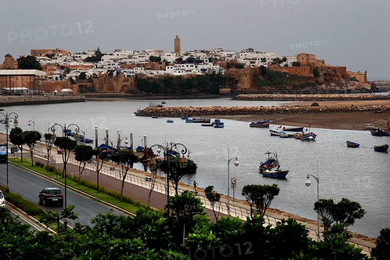 View across the river to the historic town of Salé with boats and city wall under cloudy sky, Rabat, Salé, Morocco