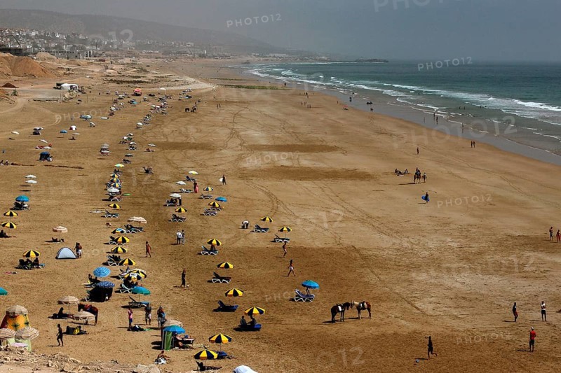 Busy sandy beach of Taghazout with lots of umbrellas and people at the sea, Taghazout, Souss-Massa region, Morocco