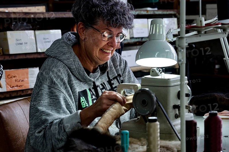 Seamstress works concentrated with thread and material under a lamp in a Possum factory, Stratford, New Zealand