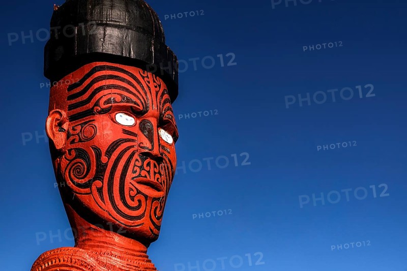 Large carved Maori figure painted red against deep blue sky in Whakarewarewa village, Rotorua, North Island, New Zealand