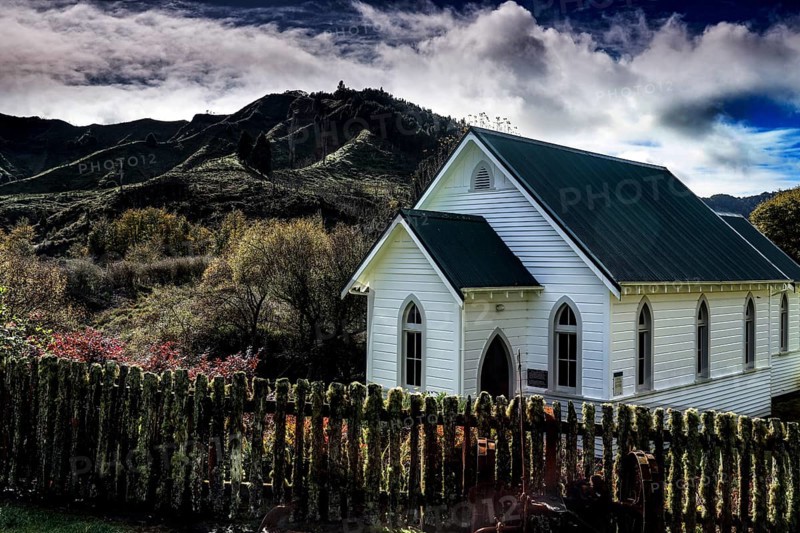 White church against wooded mountains under dramatic sky in Whangamomona, Whangamomona, New Zealand