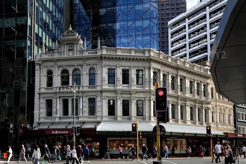 Busy intersection with historic façade contrasting with modern glass buildings on Lambton Quay, Wellington, New Zealand