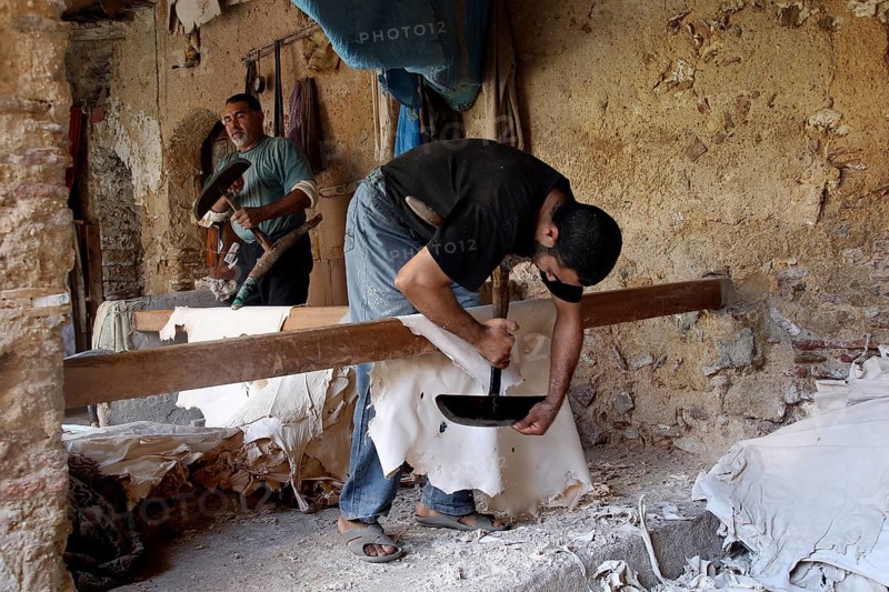A man works on leather goods in an old workshop with rustic charm, Fez, Fez el Bali, Morocco