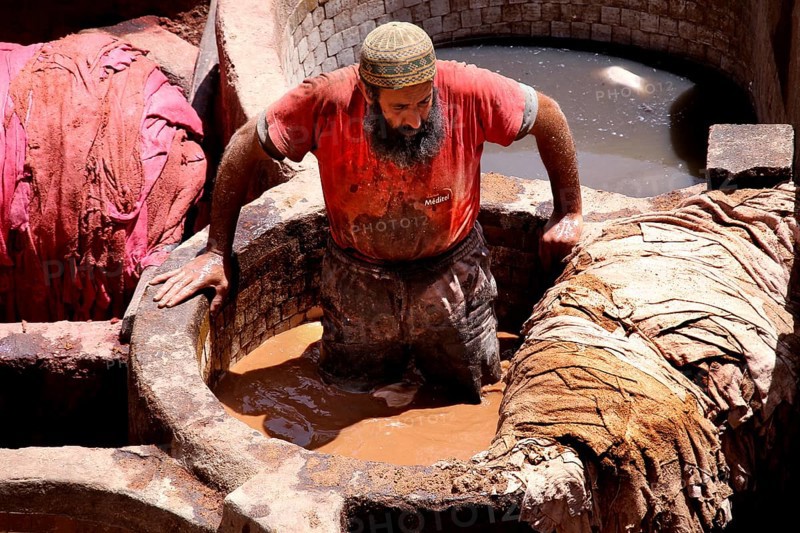 A worker in the tanners' quarter of Fez works on leather in a large paint basin, Fez, el-Bali, Chouwara, Morocco