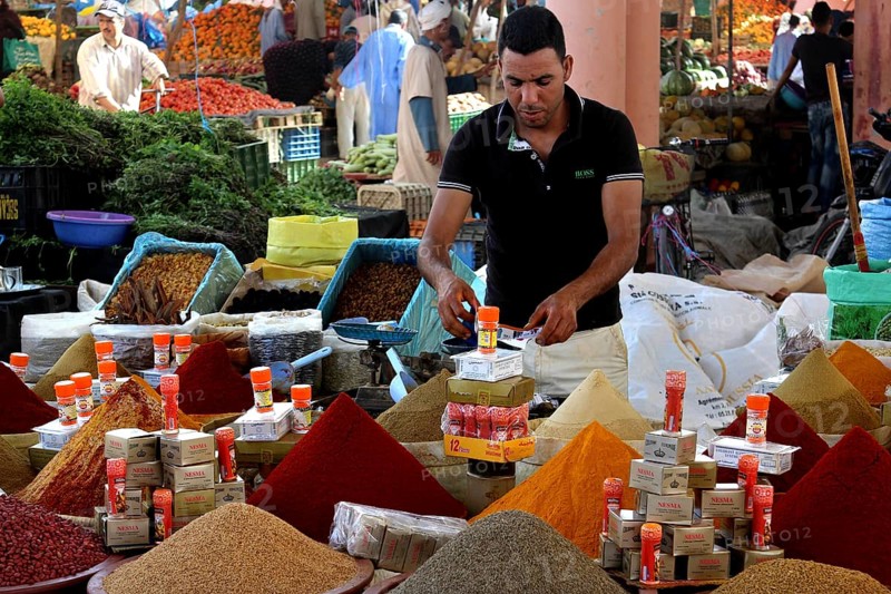 Market scene with colorful spice pyramids and a retailer presenting products, Guelmim, Morocco