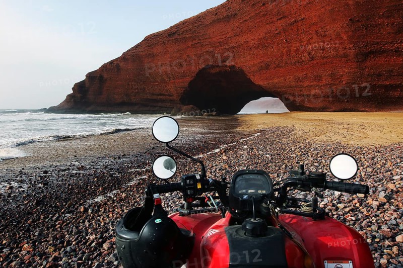Quad bike on beach with impressive rock arch in Legzira, Legzira, Morocco
