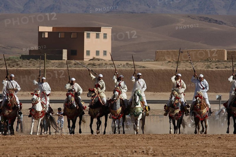 Riders in formation on a wide terrain with mountain scenery during Fantasia, El Kelâa m'Gouna, Morocco