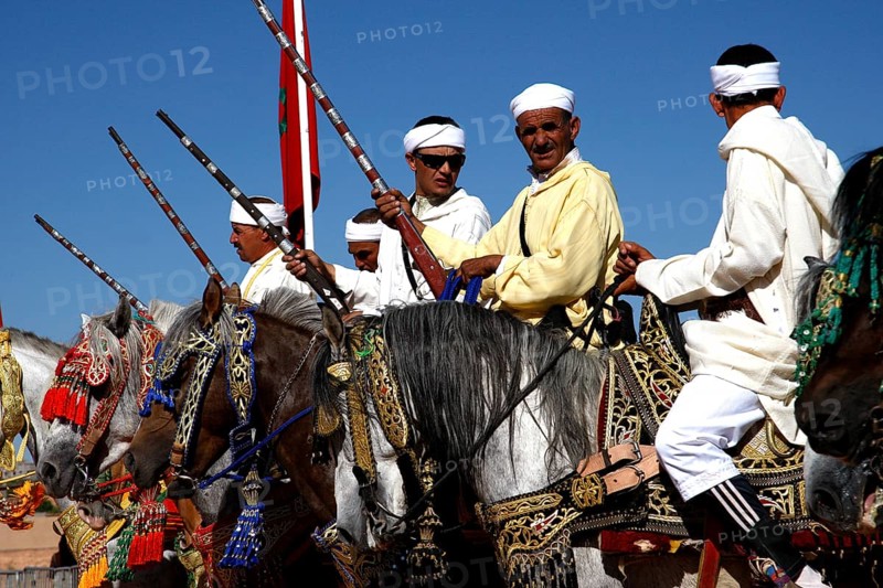 Horsemen in a group under blue skies perform a Fantasia performance, El Kelâa m'Gouna, Morocco