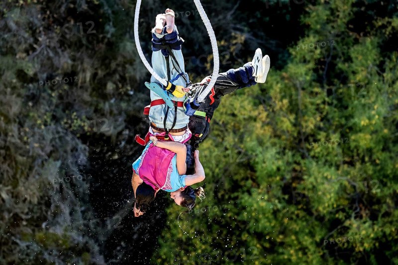 Two people in free fall bungee jumping surrounded by lush nature, Queenstown, Otago, New Zealand