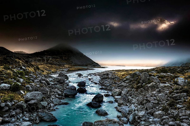Dark mountain landscape with a narrow river surrounded by boulders in the evening light, Hooker Valley Track, New Zealand