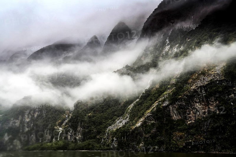 Steep, misty rocks in Milford Sound, crisscrossed by thick clouds and lush greenery, zero