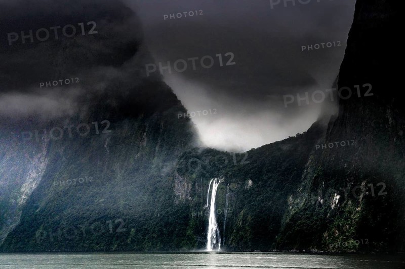 Dramatic sky over a waterfall in Milford Sound surrounded by misty mountains, zero