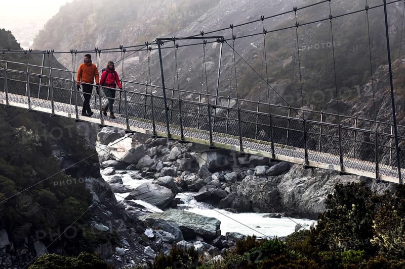 Hikers crossing a suspension bridge in a misty mountain landscape, Mt Cook, Hocker Valley Track, New Zealand
