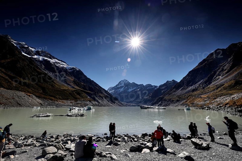 Clear sunshine over glacial lake and hikers surrounded by mountains, Mount Cook, New Zealand