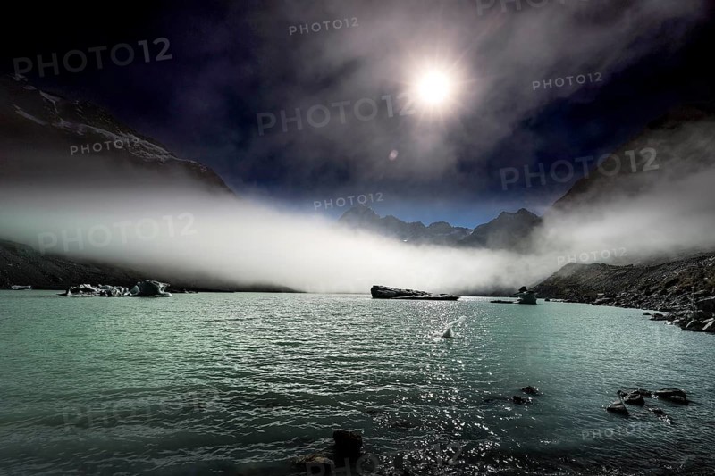 Calm glacial lake in moonlight surrounded by dramatic mountain peaks, Mount Cook, New Zealand