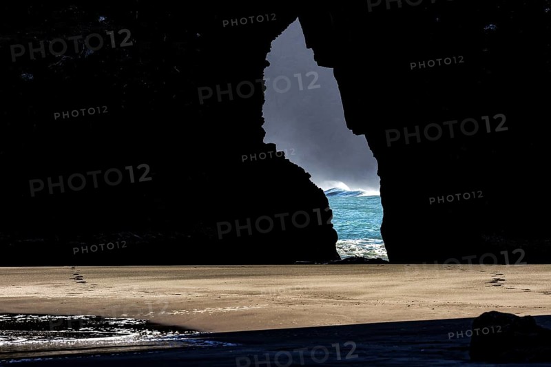 View through a crevice of the glowing sea at Piha Beach, Piha Beach, region, New Zealand