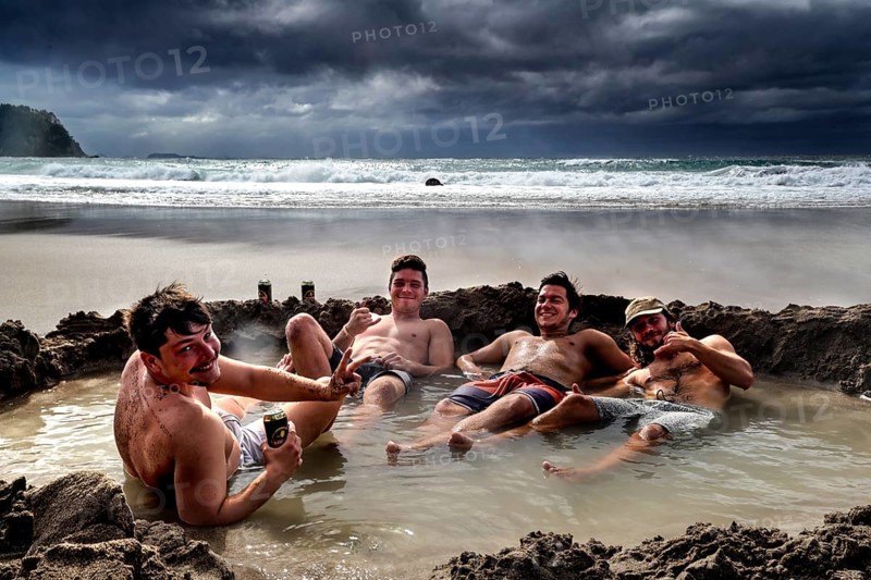 Group of men relaxing in waterhole on beach under dramatic clouds, Hot Water Beach, Coromandel Peninsula, New Zealand