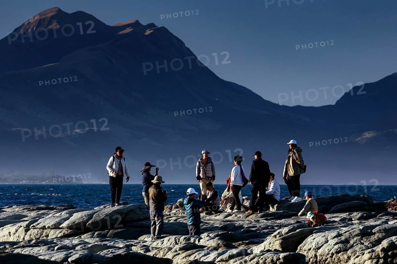 Tourists explore rocky beach with mountain views near Kaikoura, Kaikoura, New Zealand