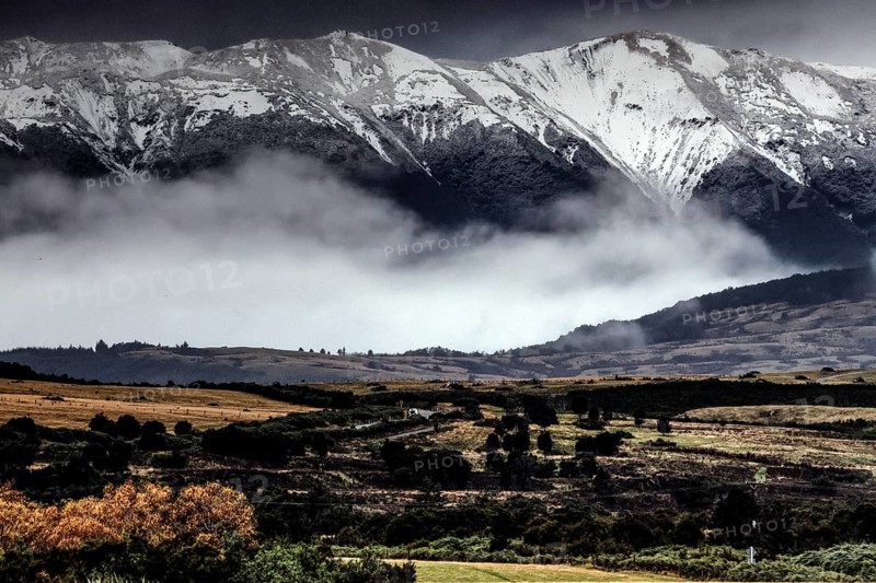 Snow-capped mountains with extensive pasture and fog, Milford Road, New Zealand