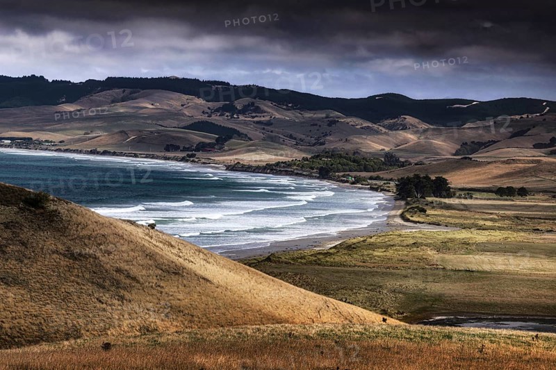 Waves break on Katiki Point beach surrounded by rolling hills, Katiki Point, New Zealand