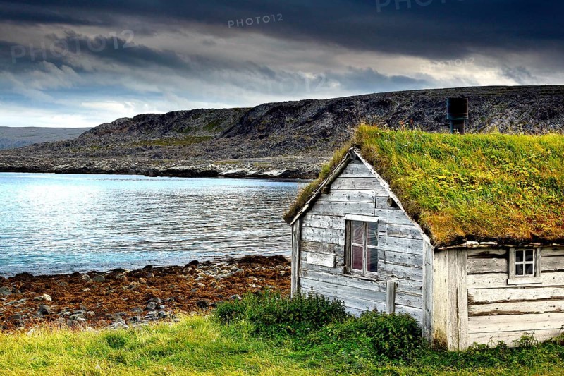 Wooden house with grass roof on the coast of Hamningberg, dramatic sky in the background