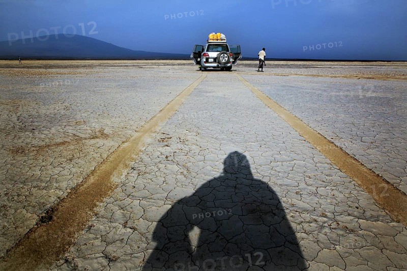 Person casting shadows in desert landscape in front of a land cruiser, Kusrawad, Ethiopia
