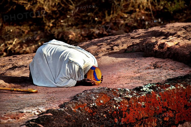 Kneeling person praying on rock, expressing deep faith near Bete Gyorgis, Lalibela, Amhara, Ethiopia