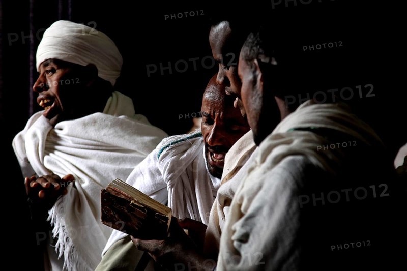 Men read Bete Gabriel and Raphael in the dark church, engrossed in prayer, Lalibela, Amhara, Ethiopia