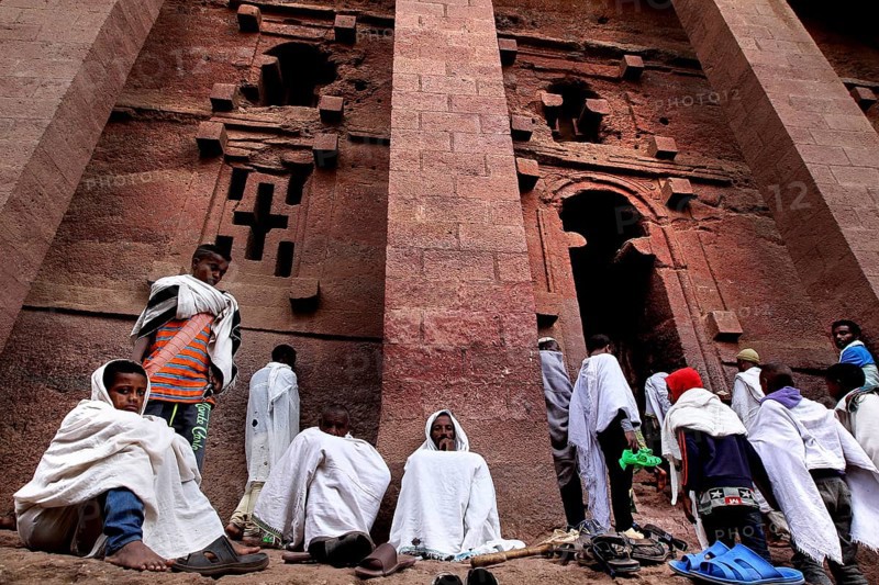 Pilgrims wearing white cloaks gather solemnly in front of the Bete Medhane Alem rock church at Easter, Lalibela, Amhara, Ethiopia