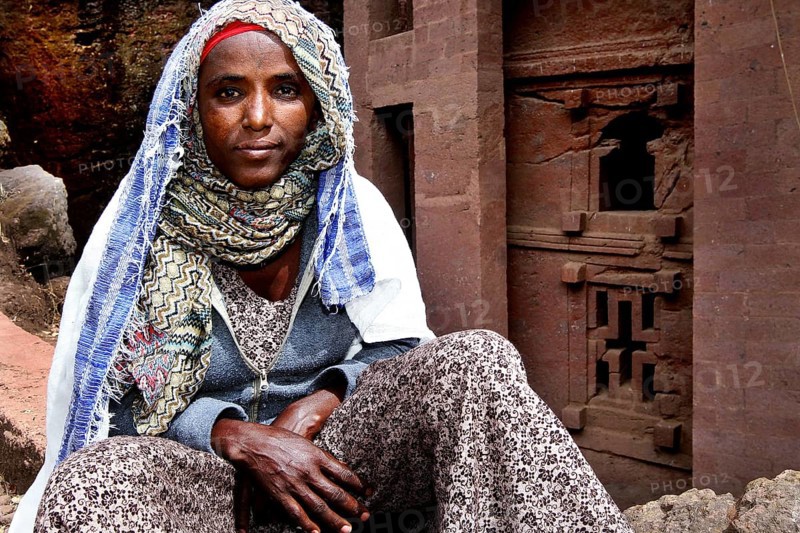 A woman sits thoughtfully in front of a traditional building, Lalibela, Amhara, Ethiopia